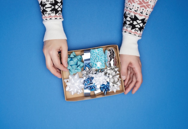 Two female hands are holding a brown cardboard box with a set of decor ribbons and bows