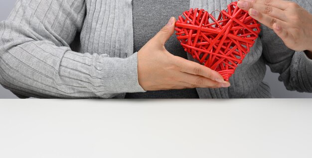 Photo two female hands are holding a red wicker heart. kindness and love concept, valentines day, banner