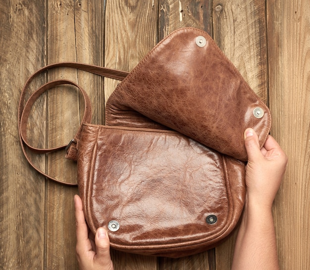 Two female hands hold a brown leather bag on a gray wooden background