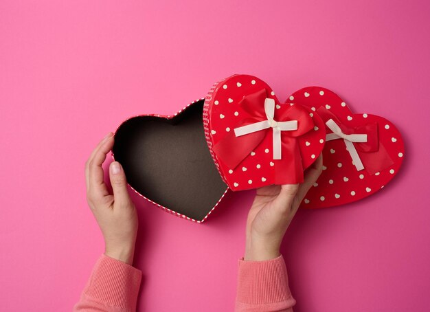 Two female hands hold a red heartshaped box on a pink background Festive backdrop