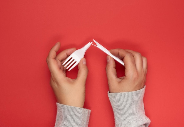 Two female hands holding halves of a plastic disposable white fork on a red background