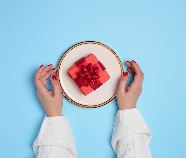 Photo two female hands holding a plate with a gift on a blue background top view