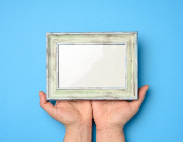 Photo two female hands holding a rectangular blank wooden frame blue background