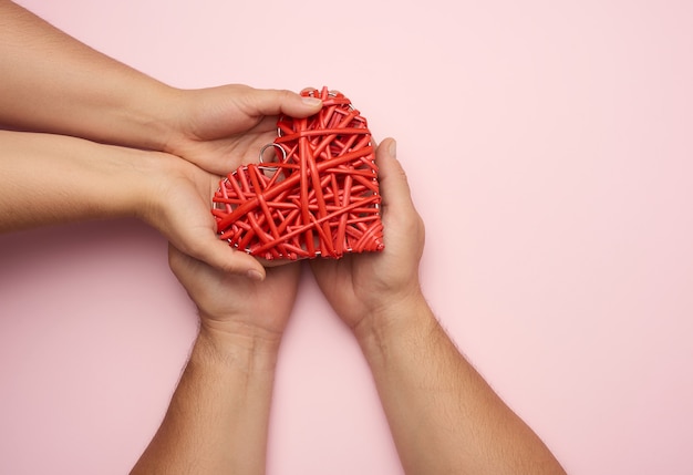 Two female hands put a red heart in men's palms. Concept of kindness, donation, top view