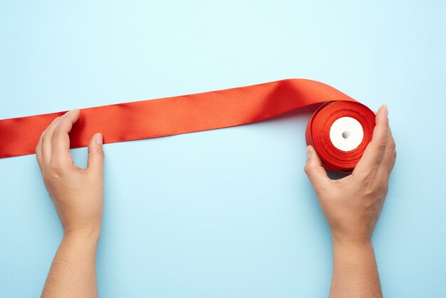 Two female hands and red silk ribbons on a blue