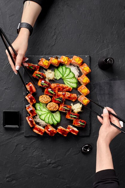 Photo two female hands using chopsticks to take rolls from sushi set