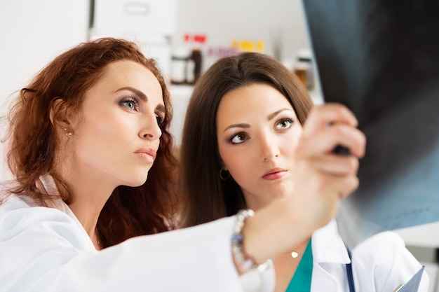 Two female medicine doctors looking at patient lungs x-ray image