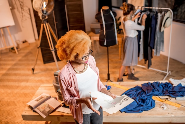 Two female multi-ethnic fashion designers working with clothes and drawings at the studiowith different tailoring tools