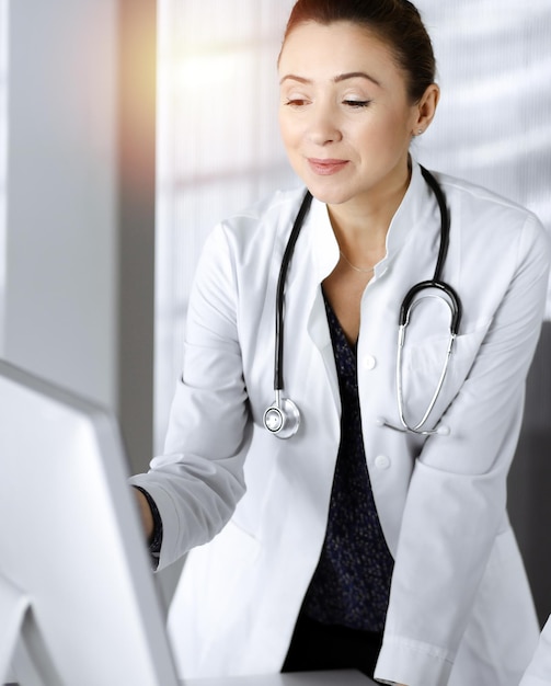 사진 두 명의 여성 의사가 햇볕이 잘 드는 진료실의 탁자에 서서 치료에 대해 논의하고 있습니다. 의사는 직장에서 pc 컴퓨터를 사용합니다. 의학의 팀워크.