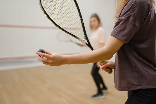 Две женщины-игроки с ракетками для сквоша, сосредотачиваются на мяч. Девочки на тренировках, активные спортивные увлечения, фитнес-тренировки для здорового образа жизни