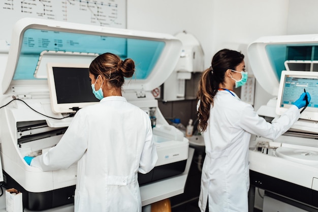 Two female scientists or technicians with face protective masks work in laboratory on human blood samples.