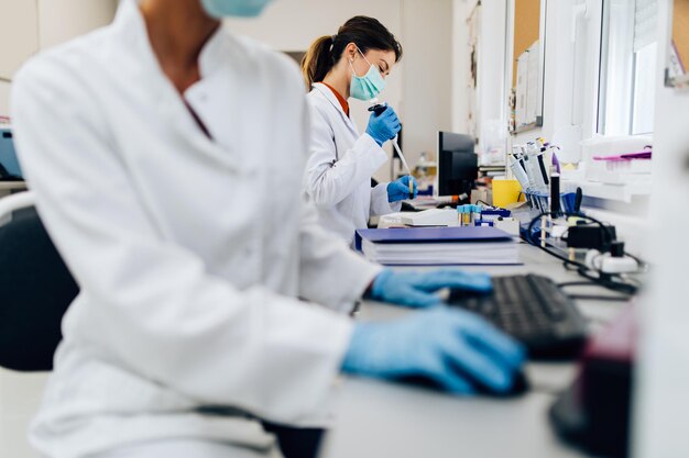 Two female scientists or technicians with face protective masks work in laboratory on human blood samples.