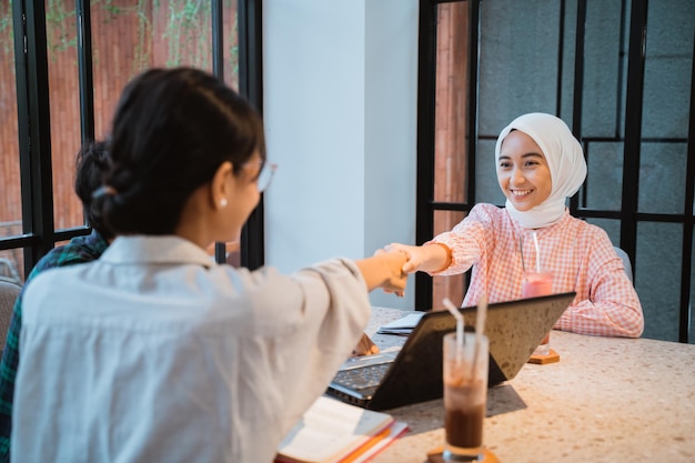 Two female students shake hands when they meet in a cafe