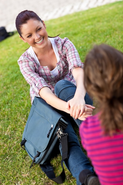 Two female students talking together sitting on the grass