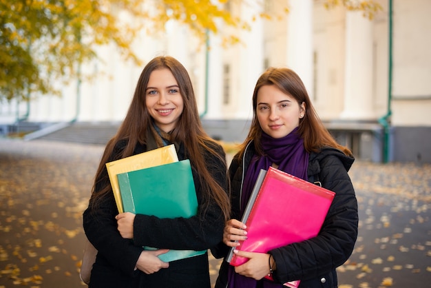 Two female students with learning materials near university building