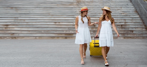 Two female twin hikers are walking near the stairs. pull a large yellow suitcase. Baner. Copy space.