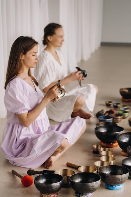 Photo two female yoga teachers play on tibetan bowls in the gym during a yoga retreat