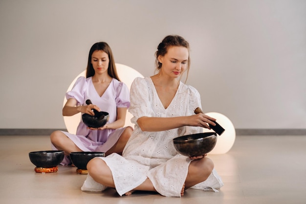 Two female yoga teachers playing a Tibetan bowl in the gym during a yoga retreat