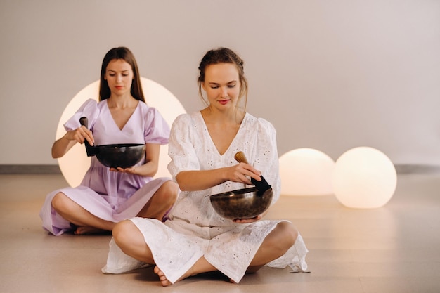 Two female yoga teachers playing a Tibetan bowl in the gym during a yoga retreat