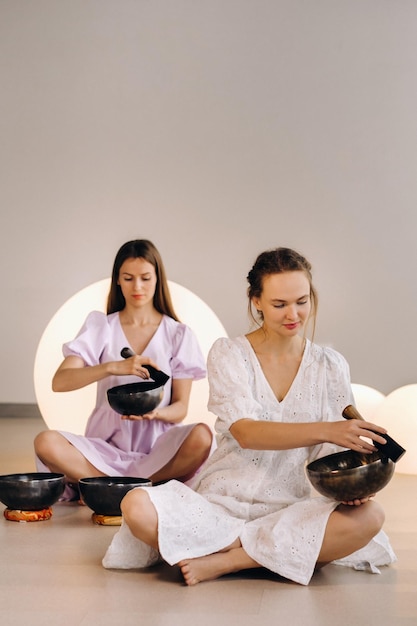 Two female yoga teachers playing a Tibetan bowl in the gym during a yoga retreat