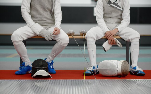 Photo two fencers sitting on the bench crop view swordsmen resting after training battle at professional swordsmanship school