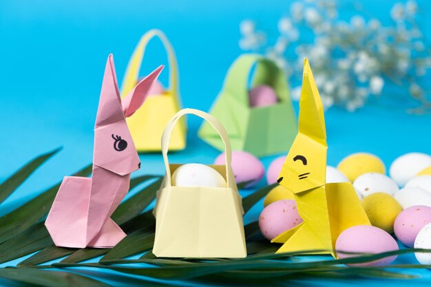 Foto due figure di conigli di pasqua fatte di carta origami e un cesto con uova su uno sfondo blu