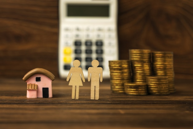 Two figures of people, a house and coins on the background of a calculator. The concept of housing acquisition. Mortgage.