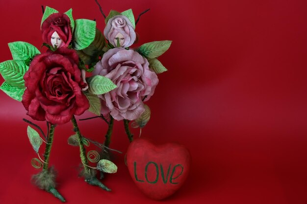 two figures in the shape of red and pink roses stand on a red background near a heart