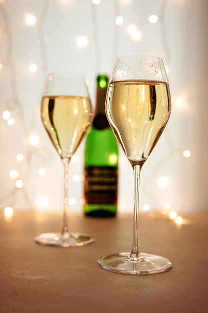 Two flute glasses of champagne or sparkling wine in a Christmas or New Year atmosphere, a bottle in the background, bokeh lights