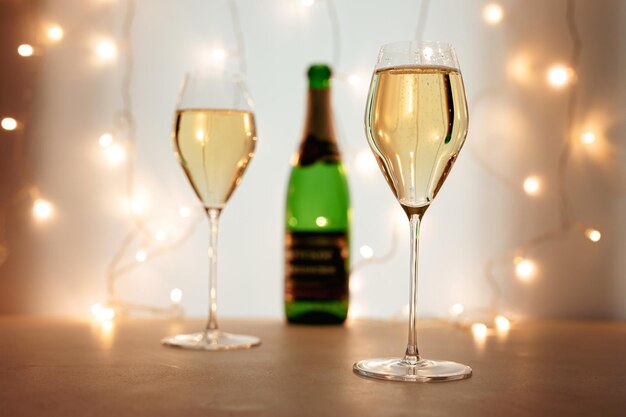 Two flute glasses of champagne or sparkling wine in a Christmas or New Year atmosphere, a bottle in the background, bokeh lights