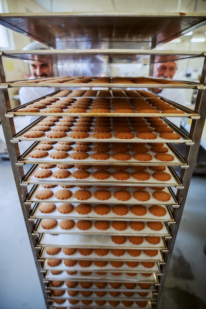 Two food plant employees pushing trays with fresh cookies. Food plant interior.