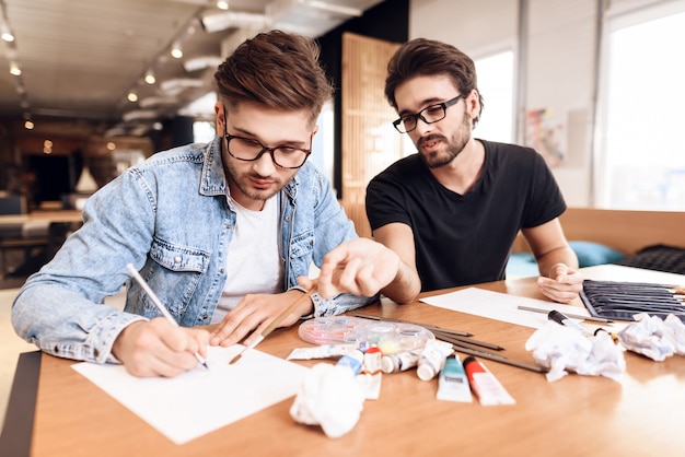 Two freelancer men drawing on paper with pencils at desk.