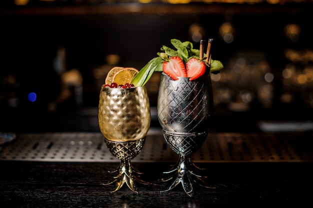 Two fresh cocktails in the pineapple form cups with strawberries and mint and berries and orange