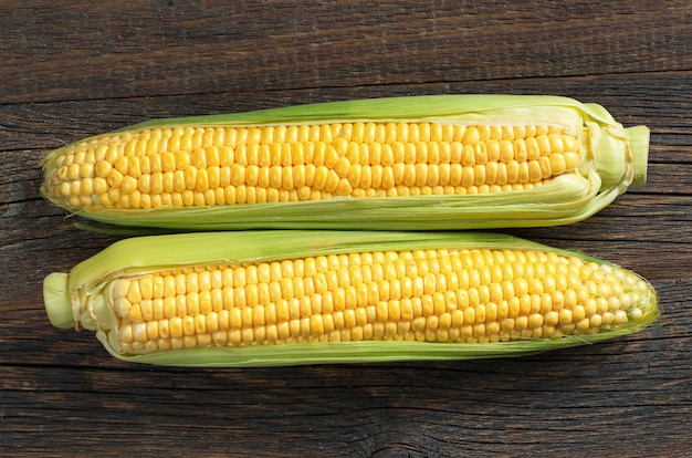 Two fresh corns on dark wooden table, top view