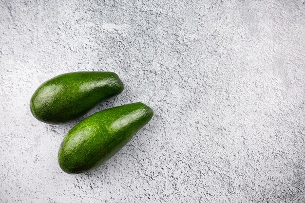 Two fresh green avocados on gray surface, top view