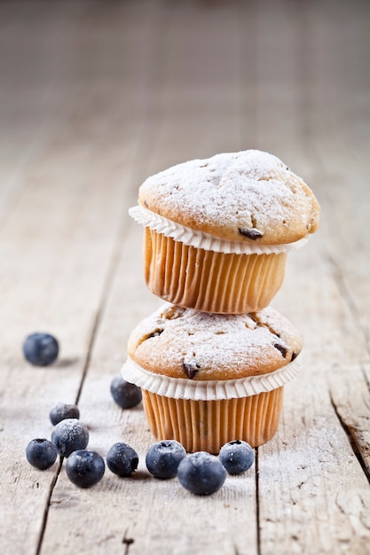 Two fresh homemade muffins with blueberries on rustic wooden table.