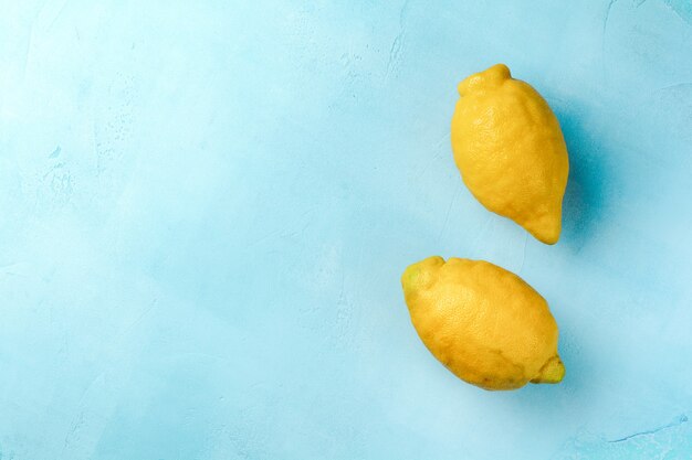 Two fresh lemons in blue plate on turquoise concrete background. Food background. Top view.