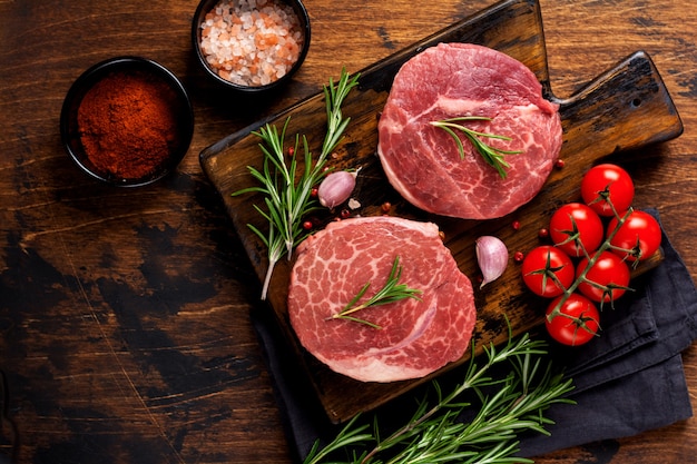 Two fresh Parisienne raw steak on wooden Board with salt, pepper and rosmary in a rustic style on old wooden background. Black angus. Top view.