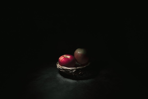 Two fresh red apples in a basket On a black background with water droplets lights are falling with space for text