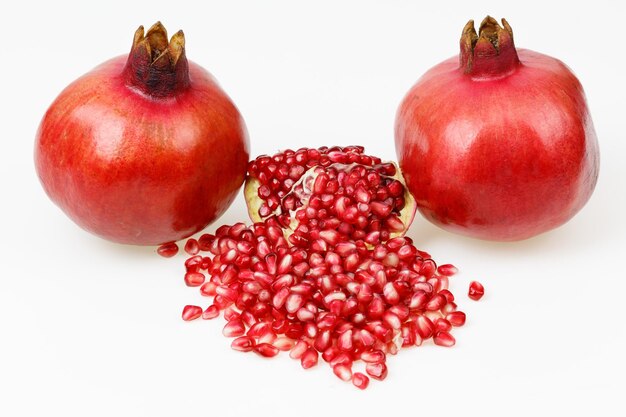 Two fresh red pomegranate fruits with one peeled piece on white background