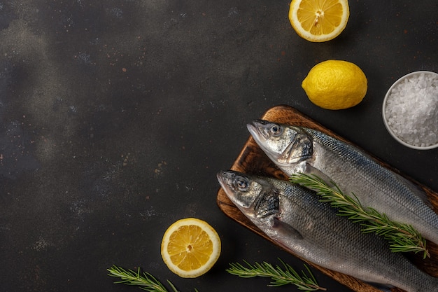 Two fresh seabass fishes with rosemary and lemon on black table