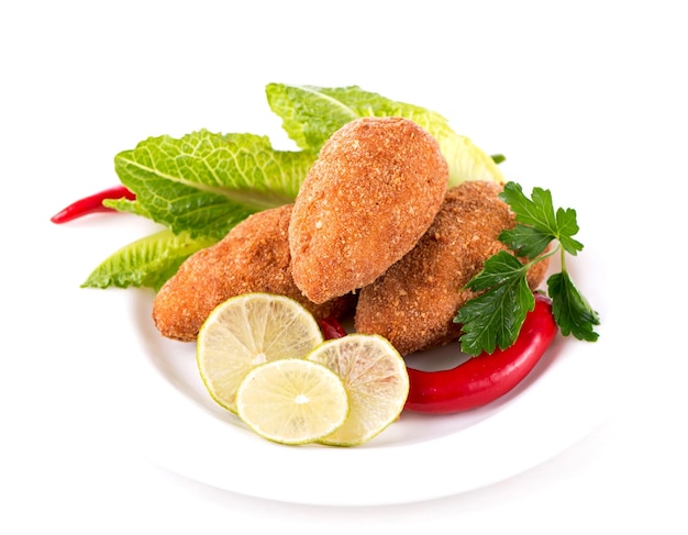 Two fried breaded cutlet with vegetables and herbs on a plate isolated on white background