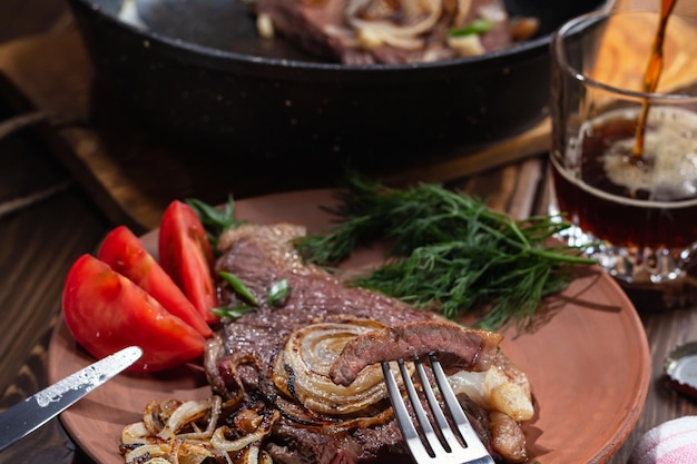 Two fried marbled Medium Well beef steaks with fried onions tomatoes dill on clay plate on wooden