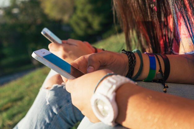 Foto due mani di amici che mandano messaggi sui loro smartphone nel parco