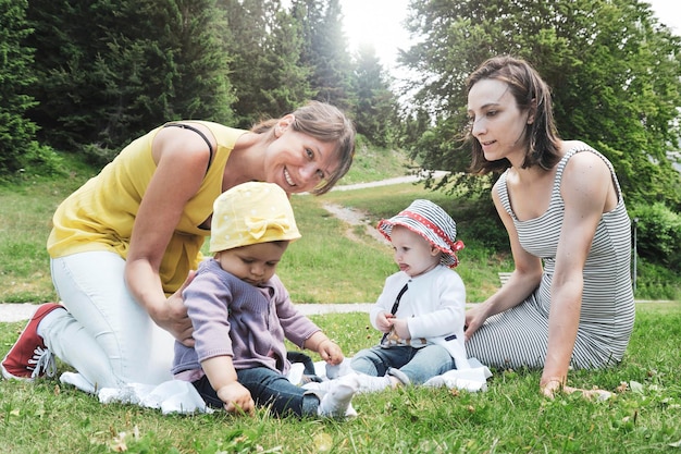 Due amiche che si godono un picnic in una bella giornata di sole con le loro piccole figlie donne sedute con bambine sull'erba nel parco di montagna concetto di maternità e vera amicizia