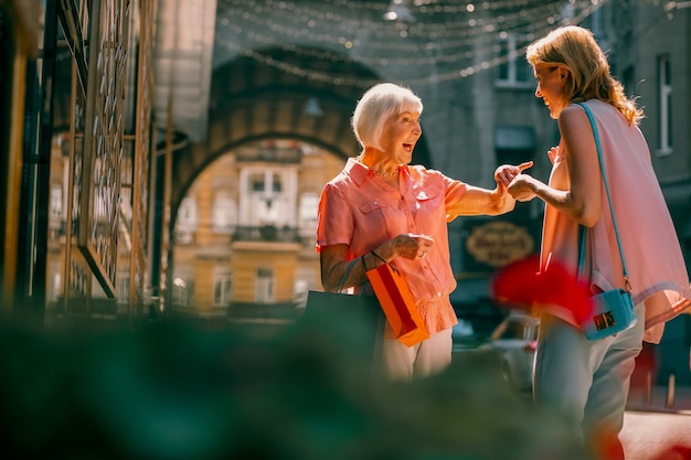 Two friendly women carrying shopping bags and smiling happily in the street to each other