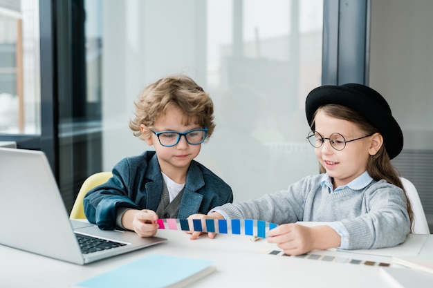 수업 시간에 책상에 앉아있는 동안 견본에서 색상을 선택하는 캐주얼웨어를 입은 두 명의 친절한 학교 어린이