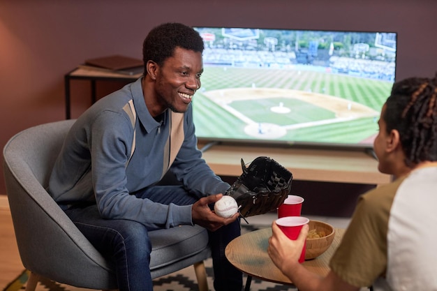 Two friends discussing baseball match at home and smiling cheerfully