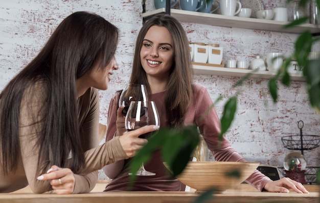 Two friends girls having a glass of red wine at the kitchen