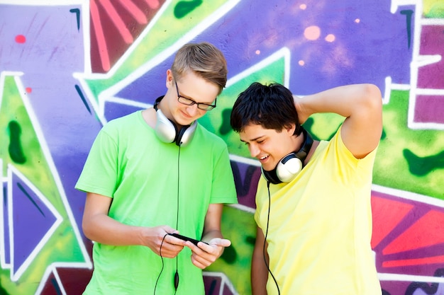 Two friends listening music near graffiti wall.